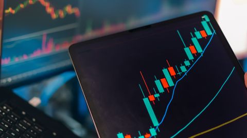 A tablet displaying a candlestick chart with a laptop screen showing stock market data for financial analysis.