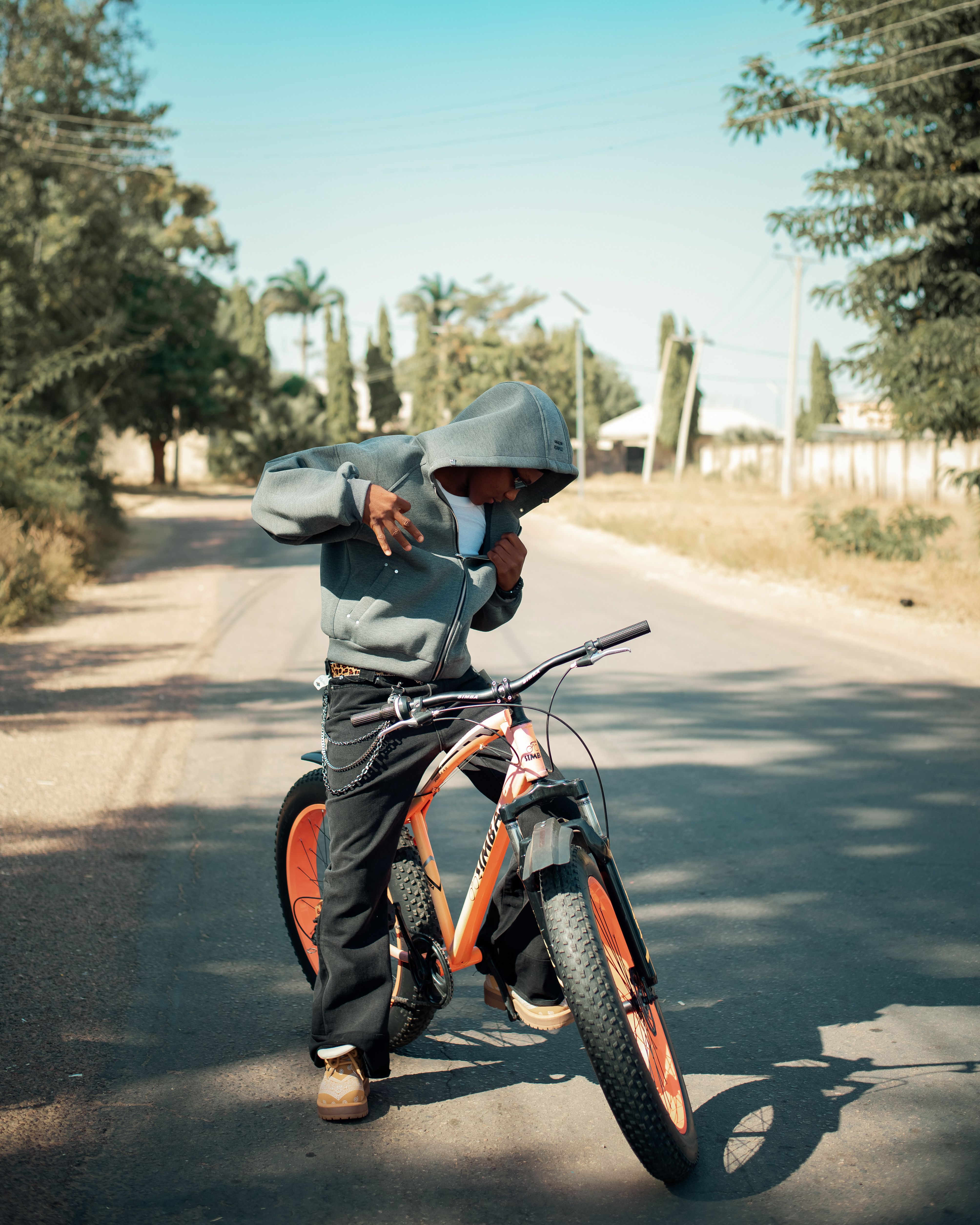 A young person poses with a bike on a clear, sunny day in a suburban street.