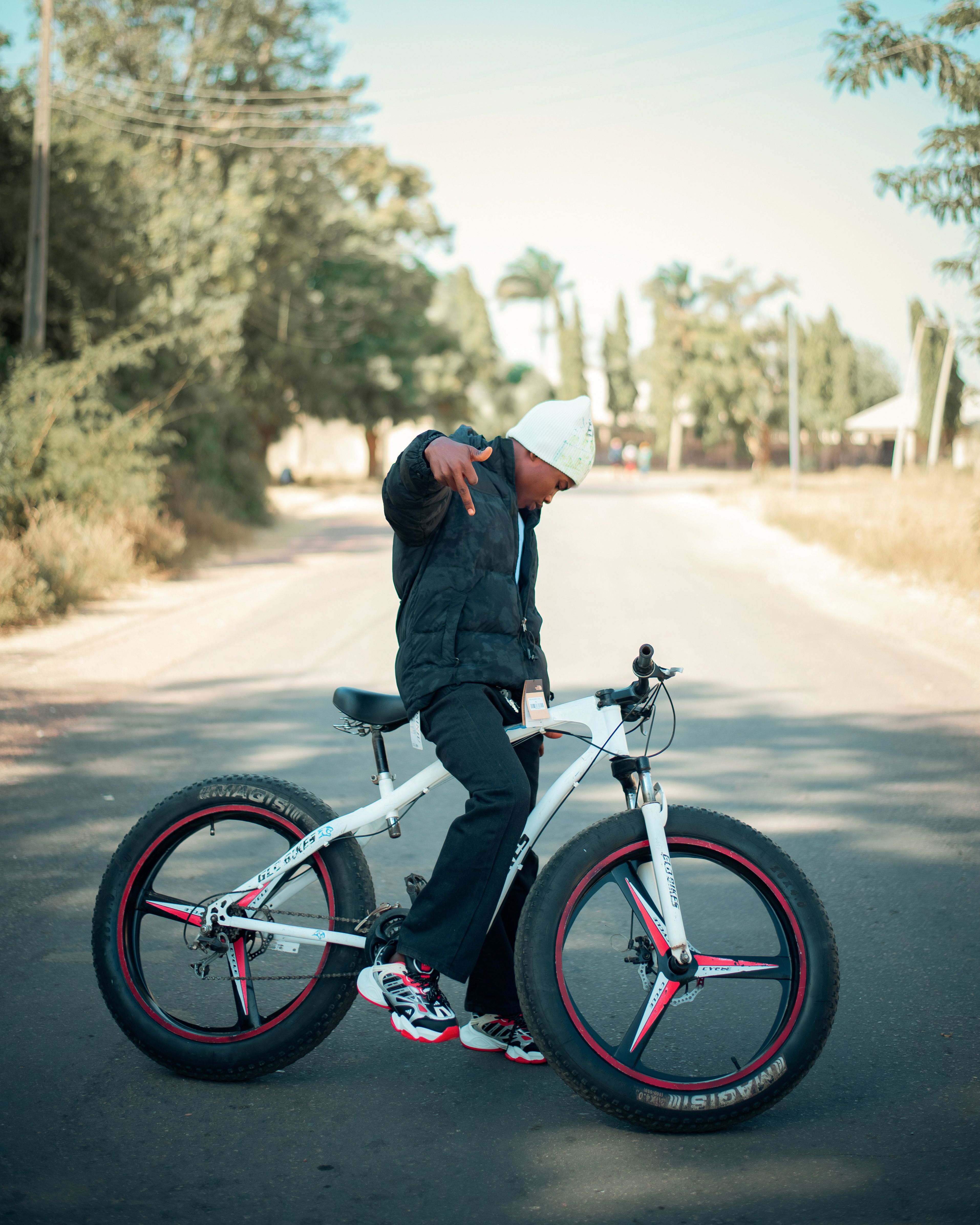 Teen wearing casual attire poses with bike on sunny urban road, showcasing a relaxed vibe.