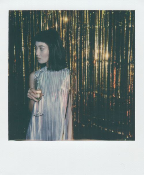 Free A woman in vintage attire holding a champagne glass against a shimmering backdrop, capturing a classic retro vibe. Stock Photo