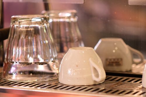 Free Close-up of an upside-down coffee cup and glass tumblers drying on an espresso machine drip tray. Stock Photo