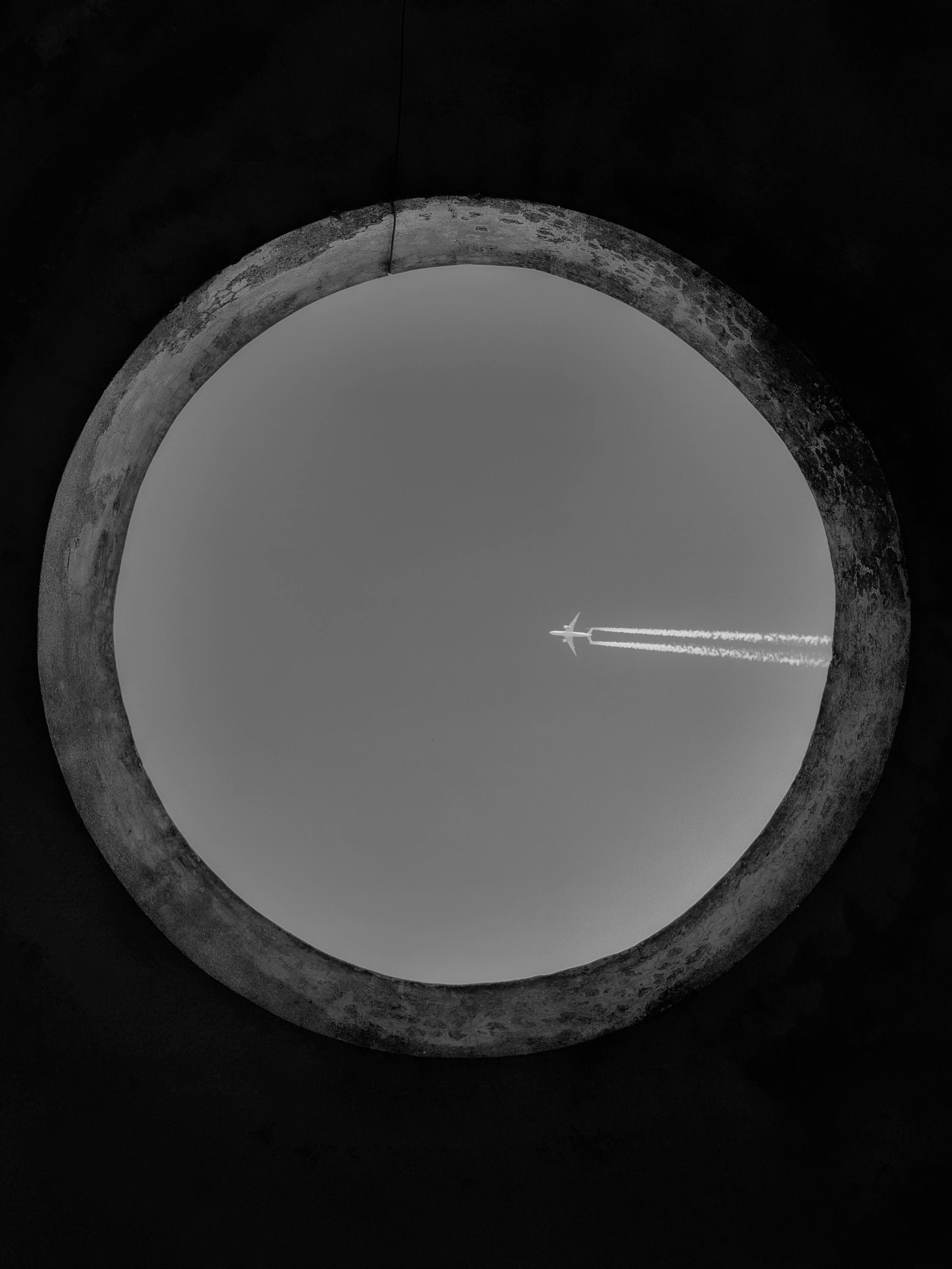 無料 空を背景にした円形の開口部から見た飛行機の白黒画像。 写真素材