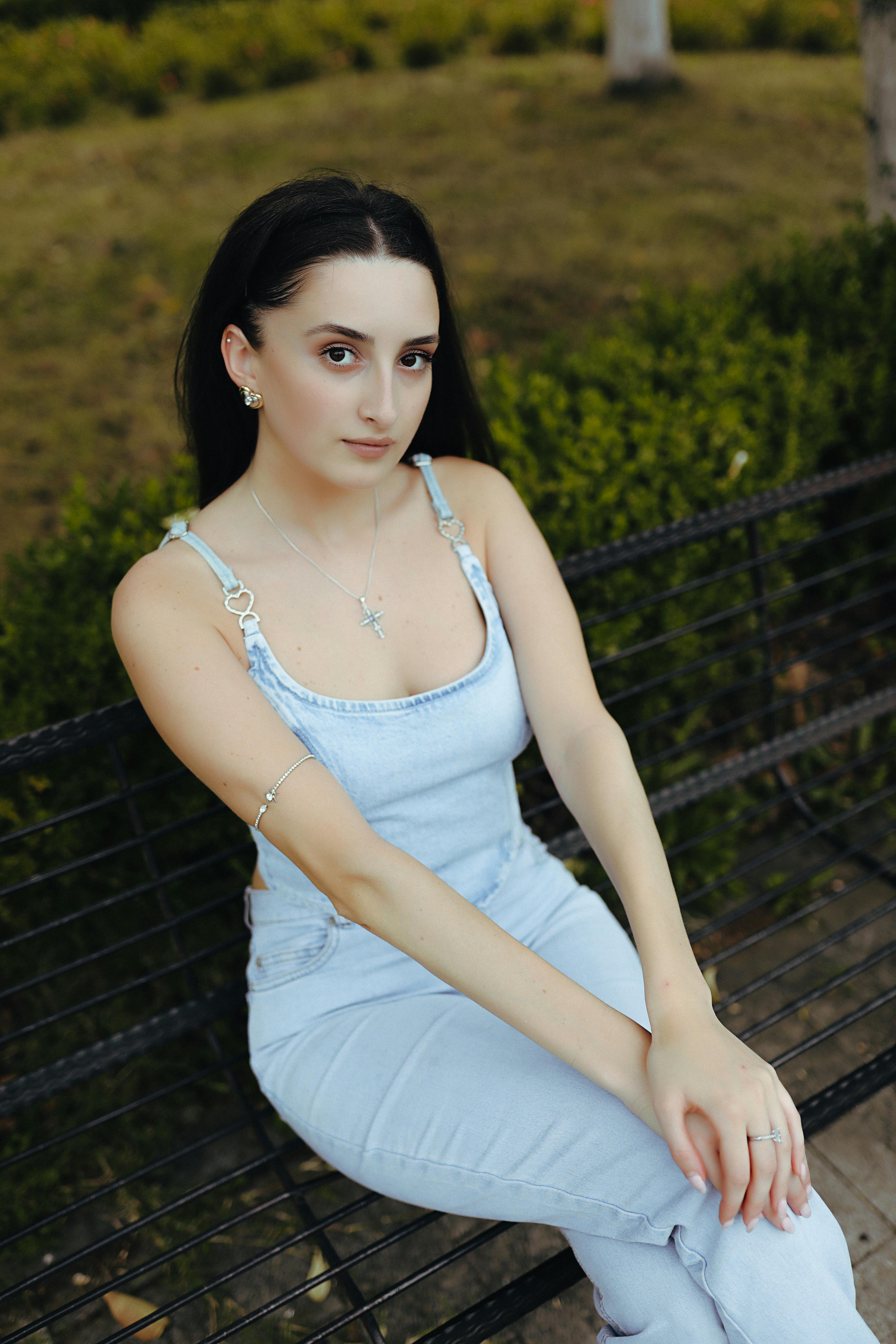 grátis Uma jovem elegante sentada em um banco no parque de Tbilisi, exibindo elegância e beleza natural. Foto profissional
