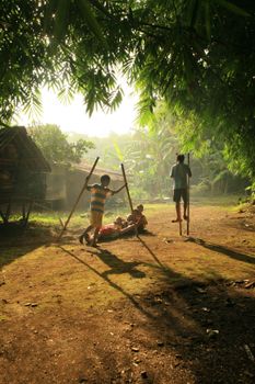 Kids enjoying stilt walking in a sunlit rural village. Vibrant and playful outdoor scene.