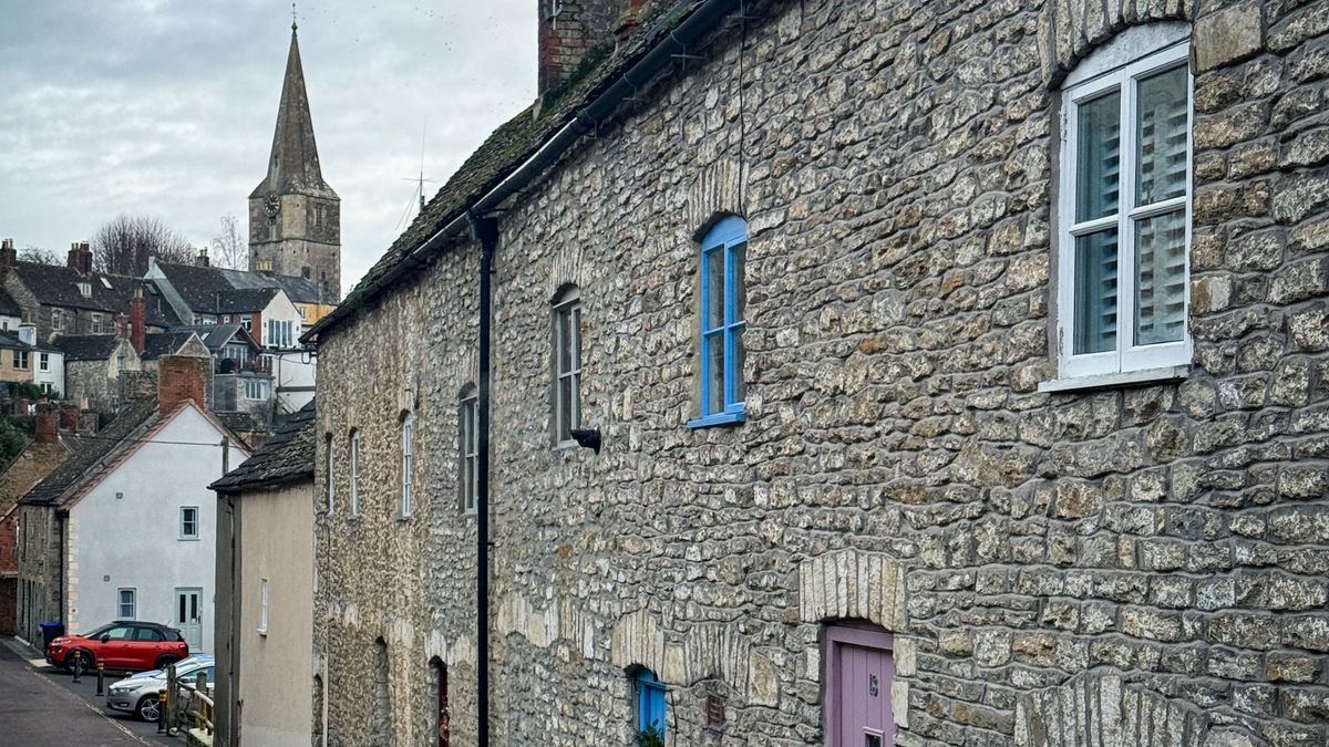 A terrace of stone cottages on a narrow street in Malmesbury with the church spire behind