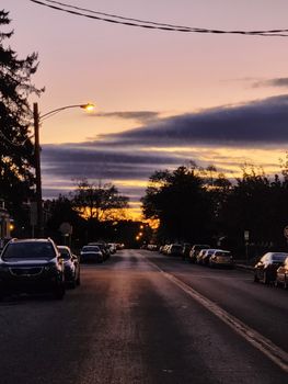 A tranquil suburban street lined with parked cars under a striking sunset sky.