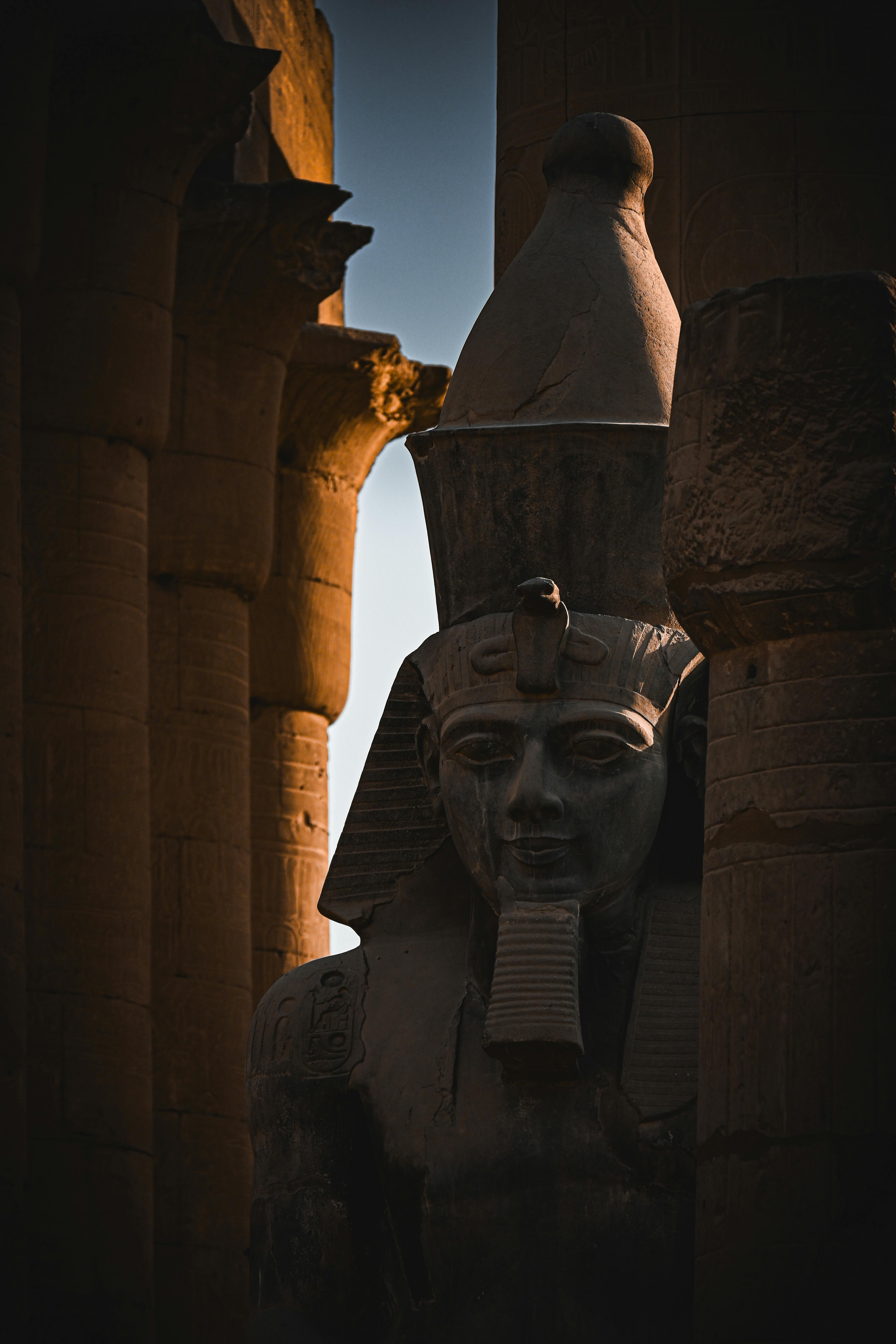 Dramatic shadow over an ancient Egyptian statue at Luxor Temple during sunset.