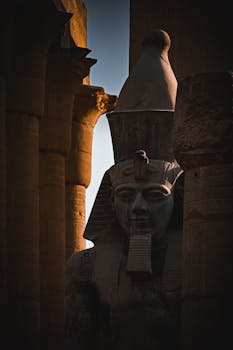 Dramatic shadow over an ancient Egyptian statue at Luxor Temple during sunset.