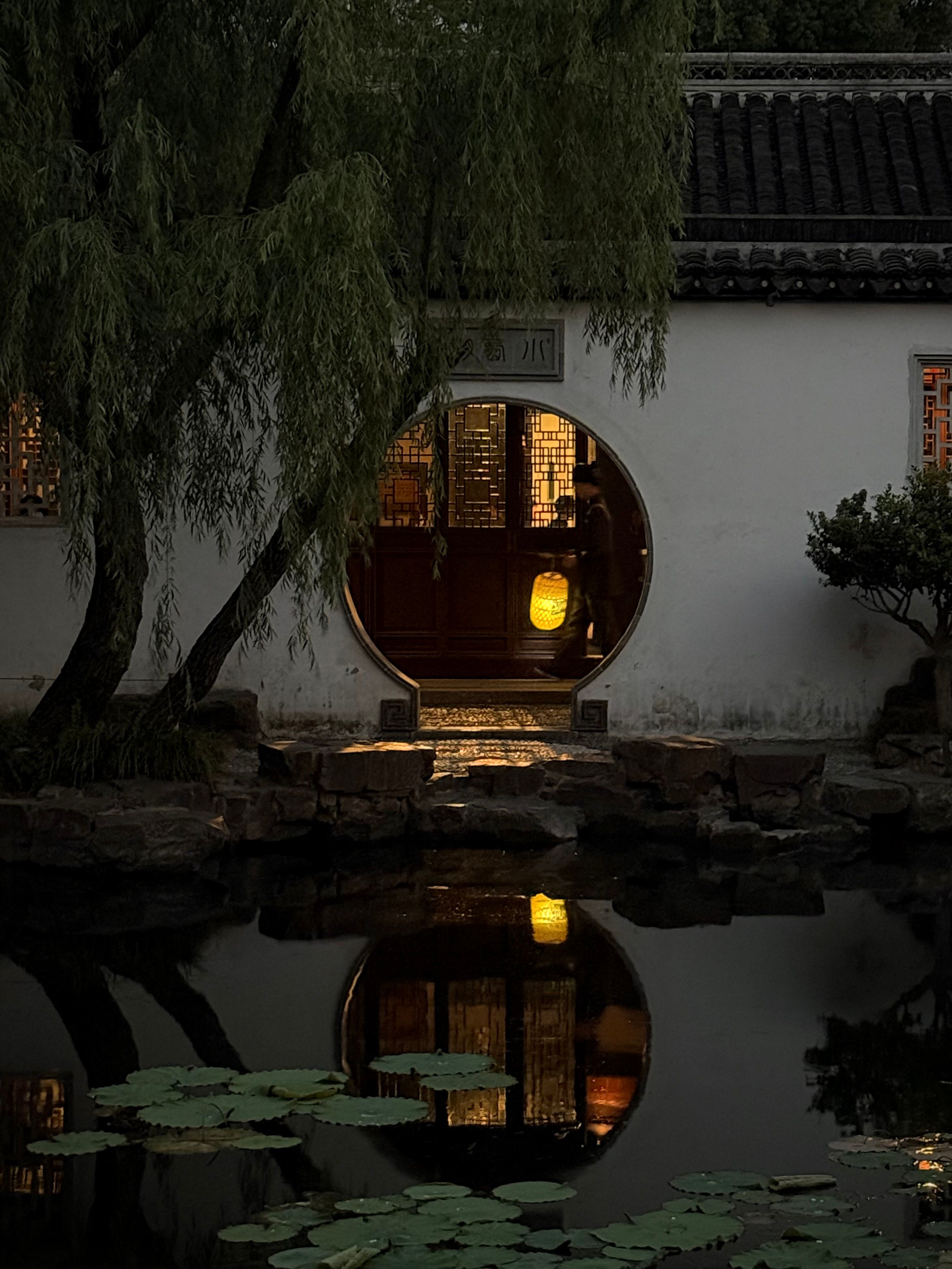 Tranquil evening view of serene Suzhou garden with illuminated lantern reflections.