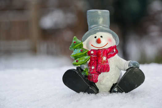 Cute snowman figurine with red scarf and green tree in snowy landscape.