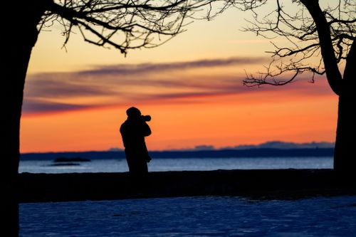 Free Silhouette of a photographer capturing a vibrant sunset by the lake. Stock Photo