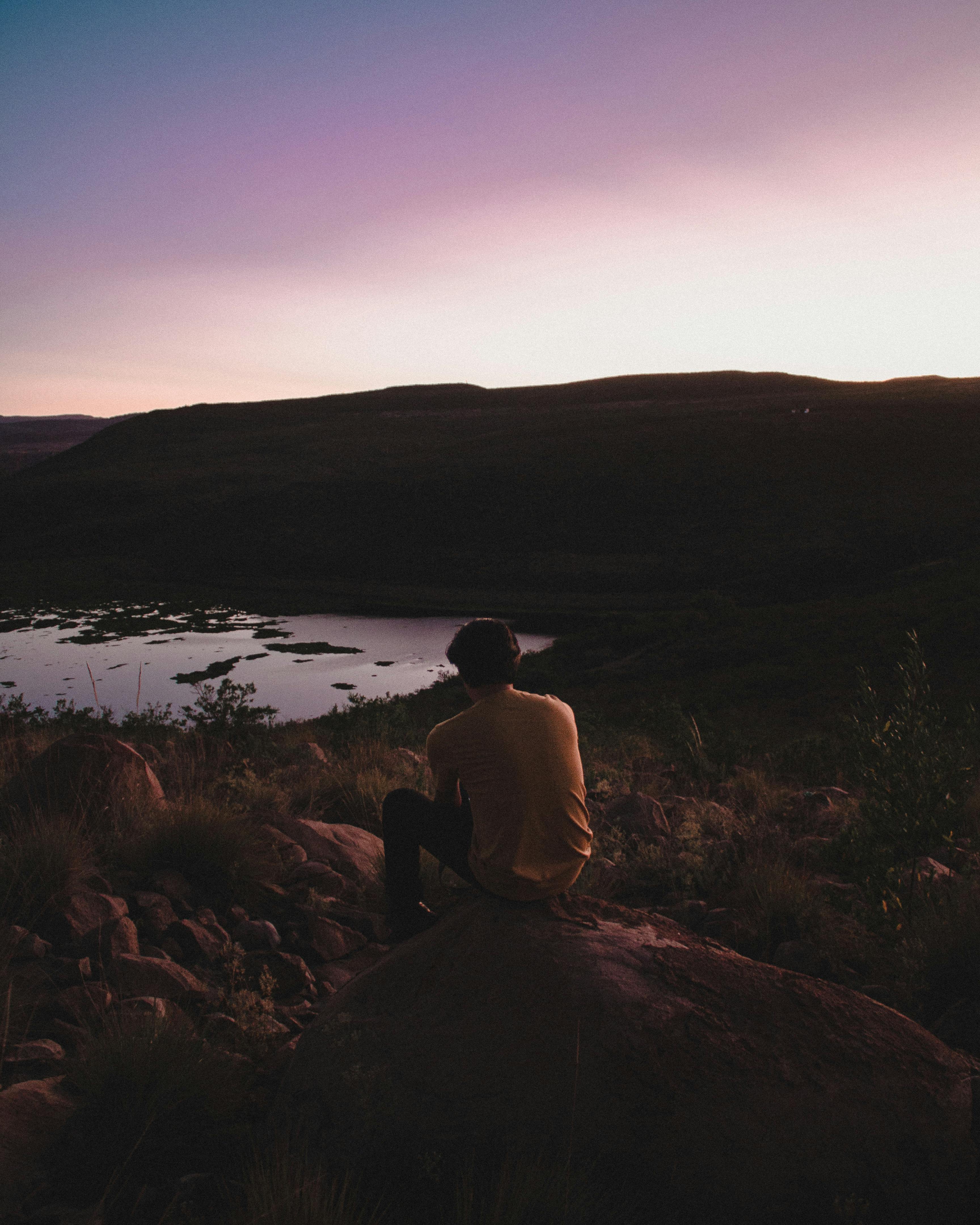 日落时分，坐在岩石上的人俯瞰着宁静的风景，四周弥漫着宁静的气氛
