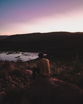 日落时分，坐在岩石上的人俯瞰着宁静的风景，四周弥漫着宁静的气氛