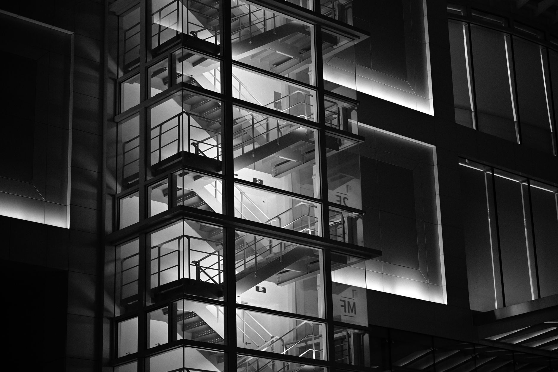 A striking black and white image of a modern glass-encased staircase in a building at night.