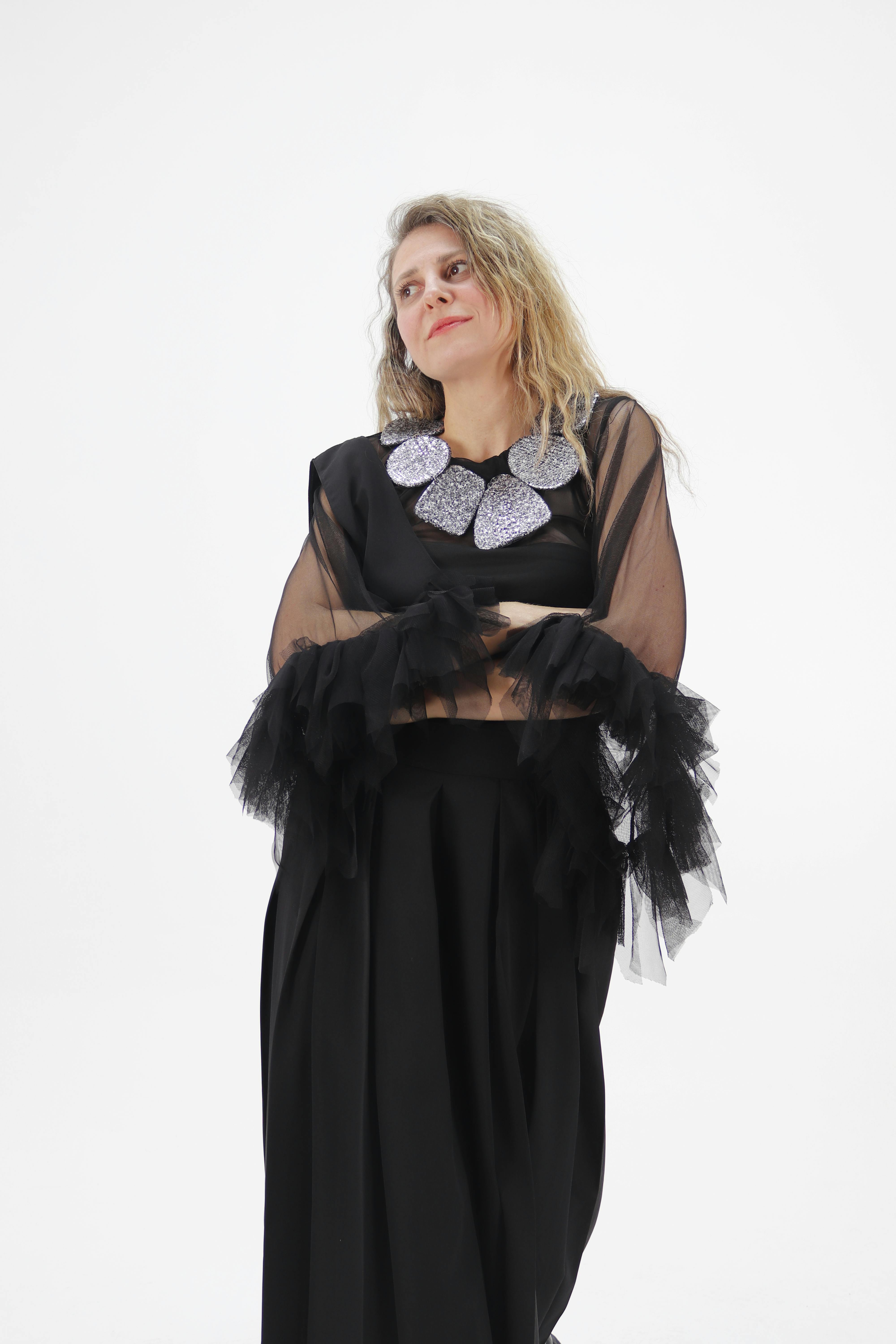 Gratis Una elegante modelo femenina adulta posa con un traje negro transparente y un collar llamativo sobre un fondo blanco. Foto de stock