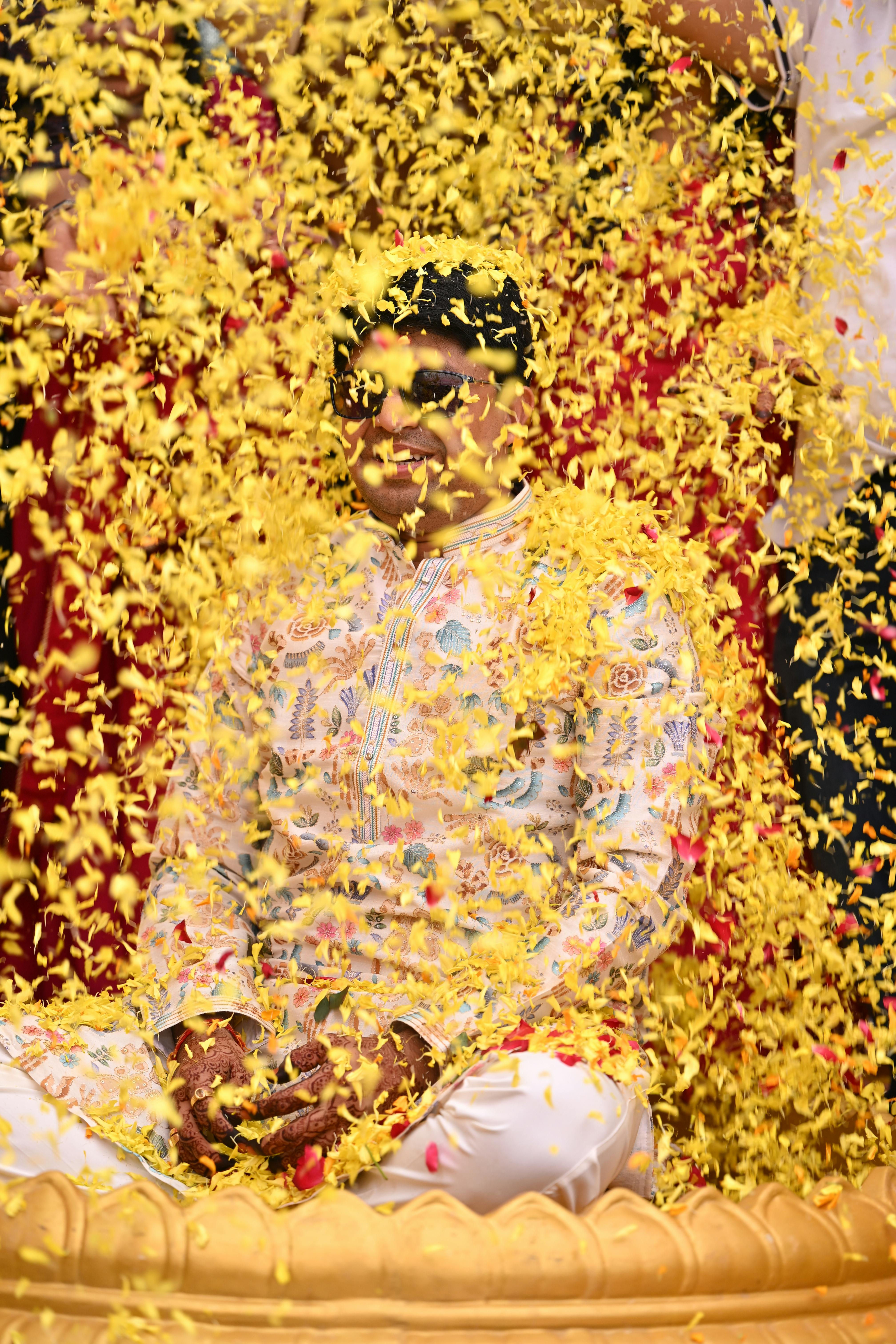 Man in traditional attire showered with vibrant flower petals during a festive celebration.
