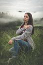 薄雾笼罩的田野里，一位年轻女子摆出姿势，展现休闲时尚与自然之美