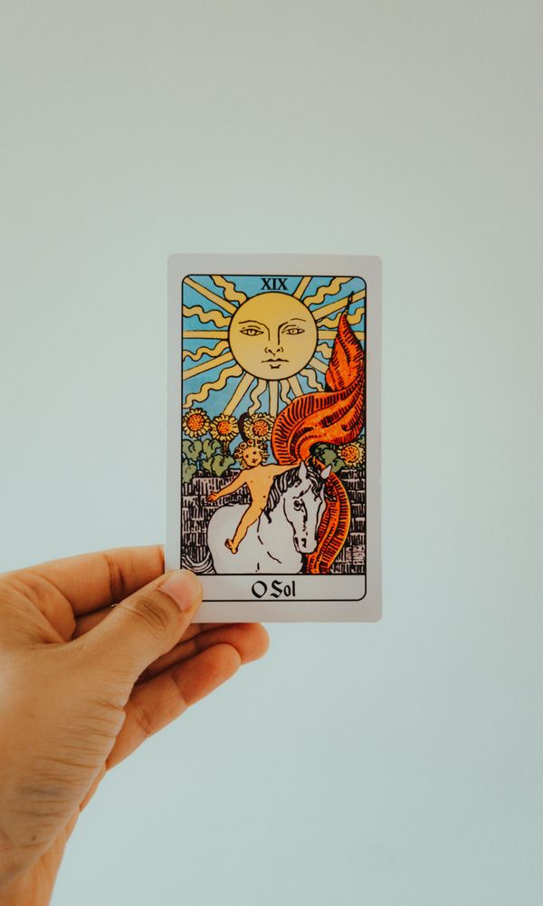 Free Close-up view of a hand holding a colorful The Sun tarot card against a minimal background. Stock Photo