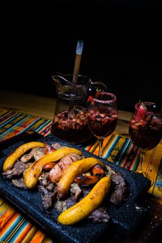 Grilled meats with plantains served beside fruity sangria on a vibrant table setting.