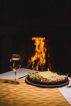A cozy dinner setup with food and wine by a warm fireplace, perfect for a romantic evening.