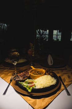 Elegant gourmet meal setup in a dimly lit restaurant, featuring rice, steak, and wine.