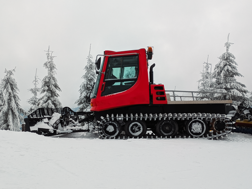 A red snowcat vehicle prepares ski slopes on a snowy mountain landscape.