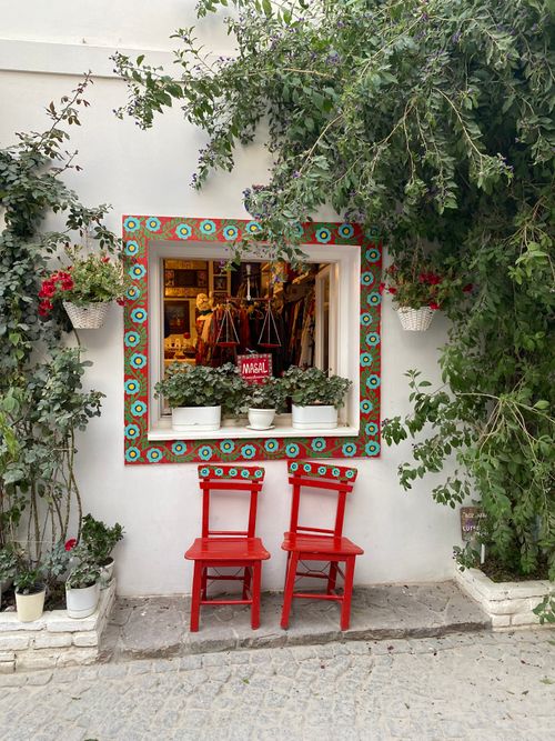 Free Colorful window display in Bozcaada, Türkiye with red chairs and vibrant greenery. Stock Photo