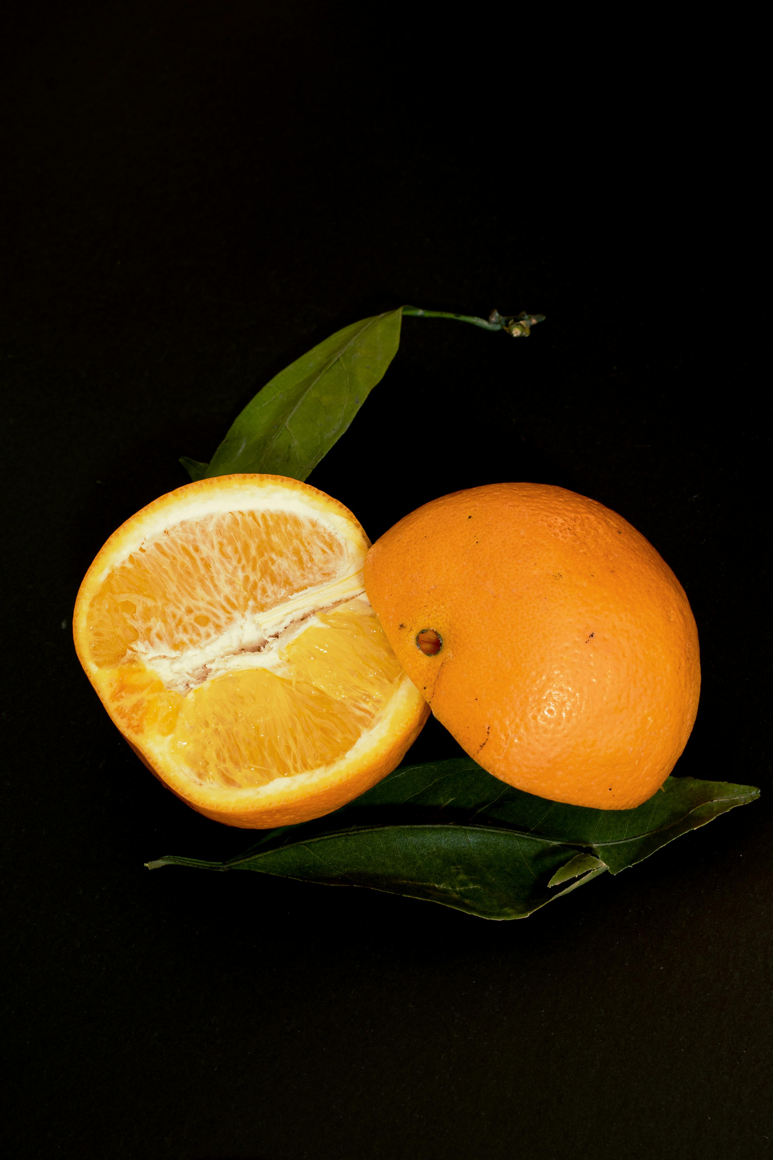 Kostnadsfria Närbild av en skivad apelsin med gröna blad mot en mörk bakgrund. Perfekt för hälsosamma matteman. Stock foto