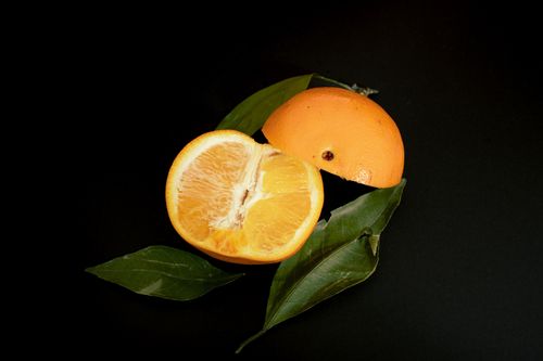 Free Juicy sliced orange on black backdrop, accompanied by vibrant green leaves, highlighting natural freshness. Stock Photo