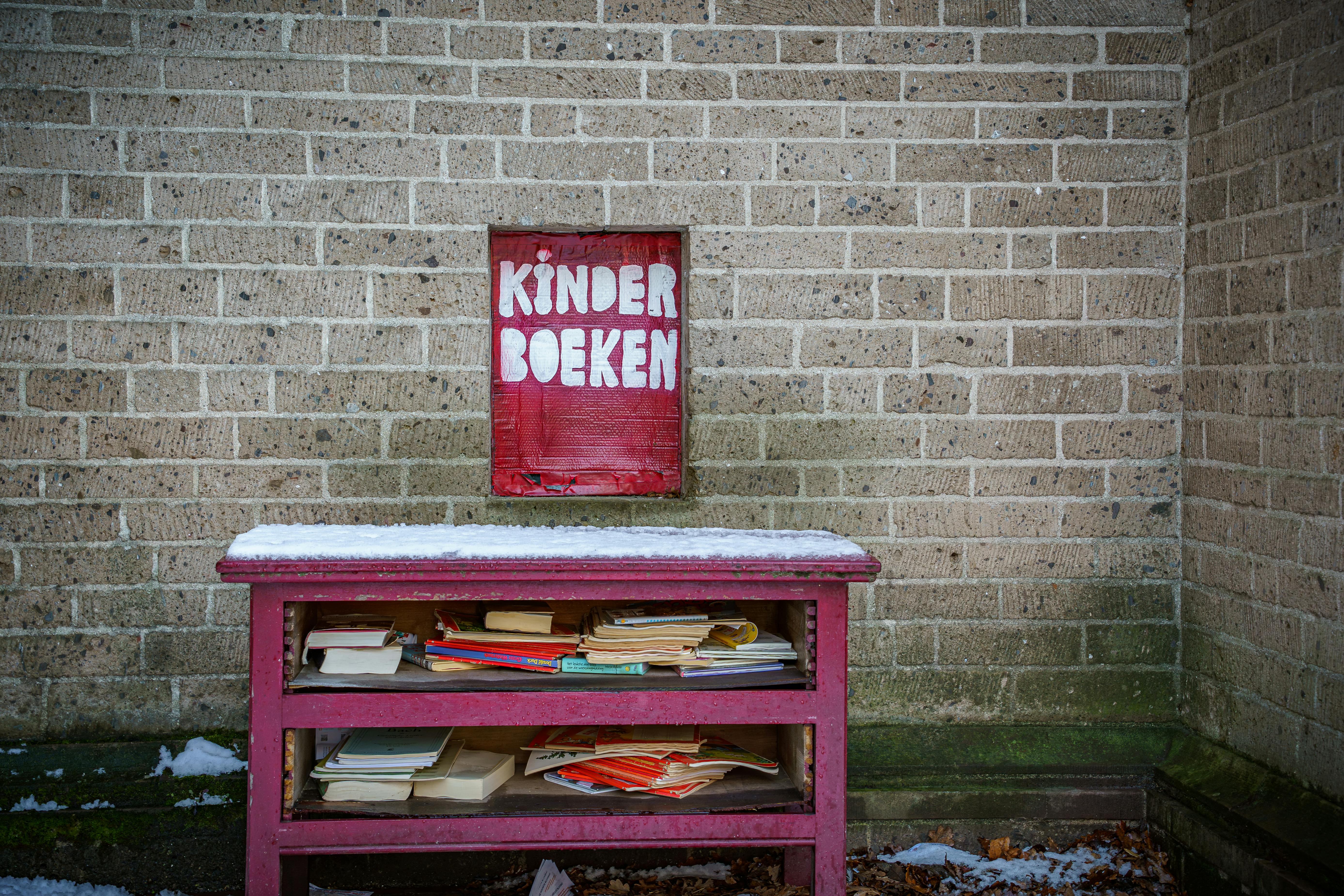 Miễn phí Giá sách màu đỏ với những cuốn sách thiếu nhi có nhãn 'Kinder Boeken' đặt cạnh bức tường gạch vào mùa đông. Ảnh lưu trữ