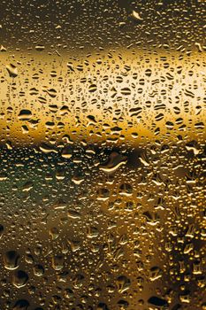Close-up of raindrops on a glass window with a golden bokeh effect