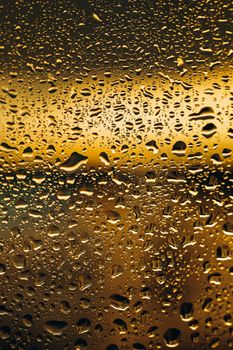 Close-up of water droplets on a window with a golden sunset backdrop, creating a calming ambiance.