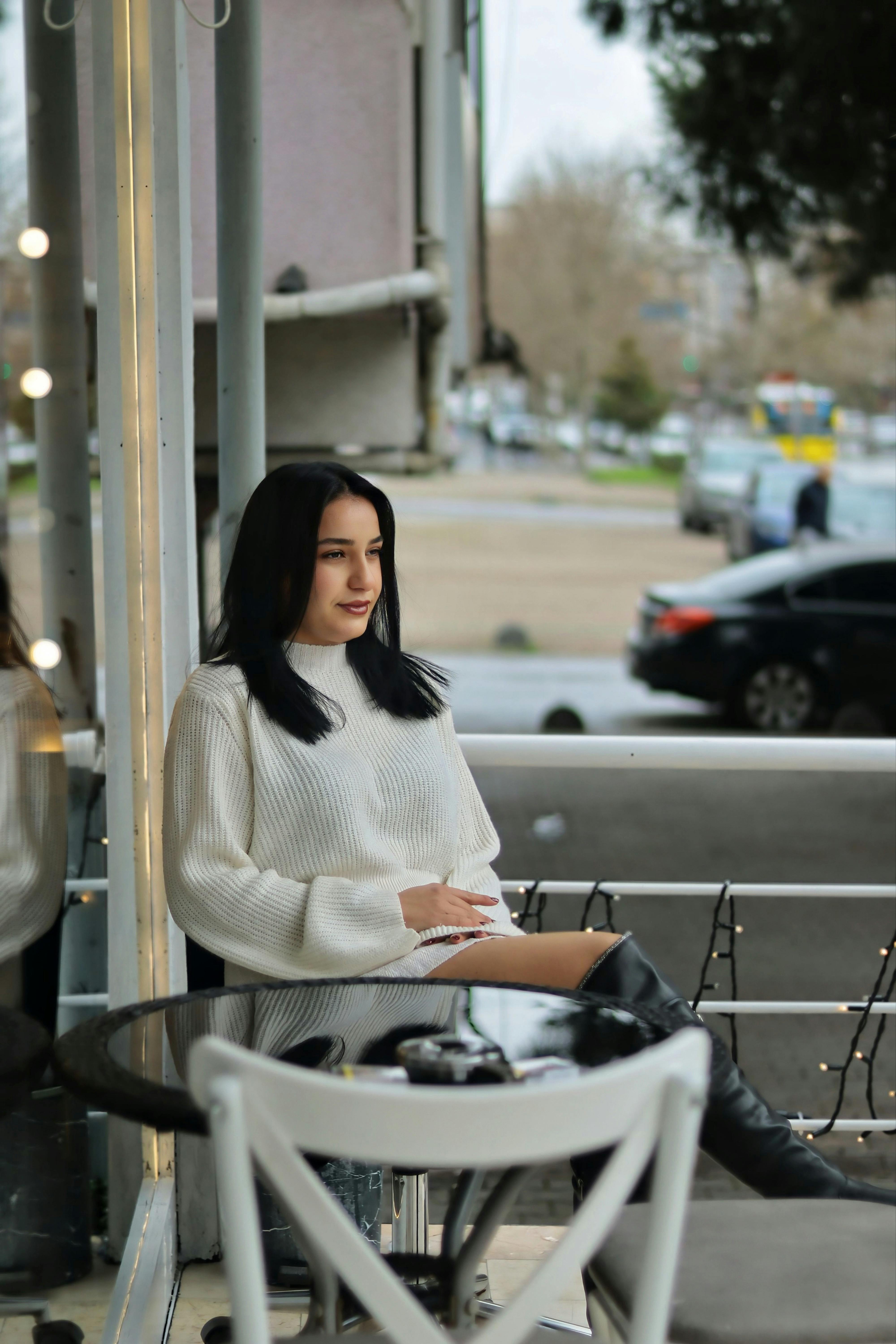 De franc Una dona jove amb un jersei blanc gaudeix d'un moment de tranquil·litat en una cafeteria a l'aire lliure. Foto d'estoc