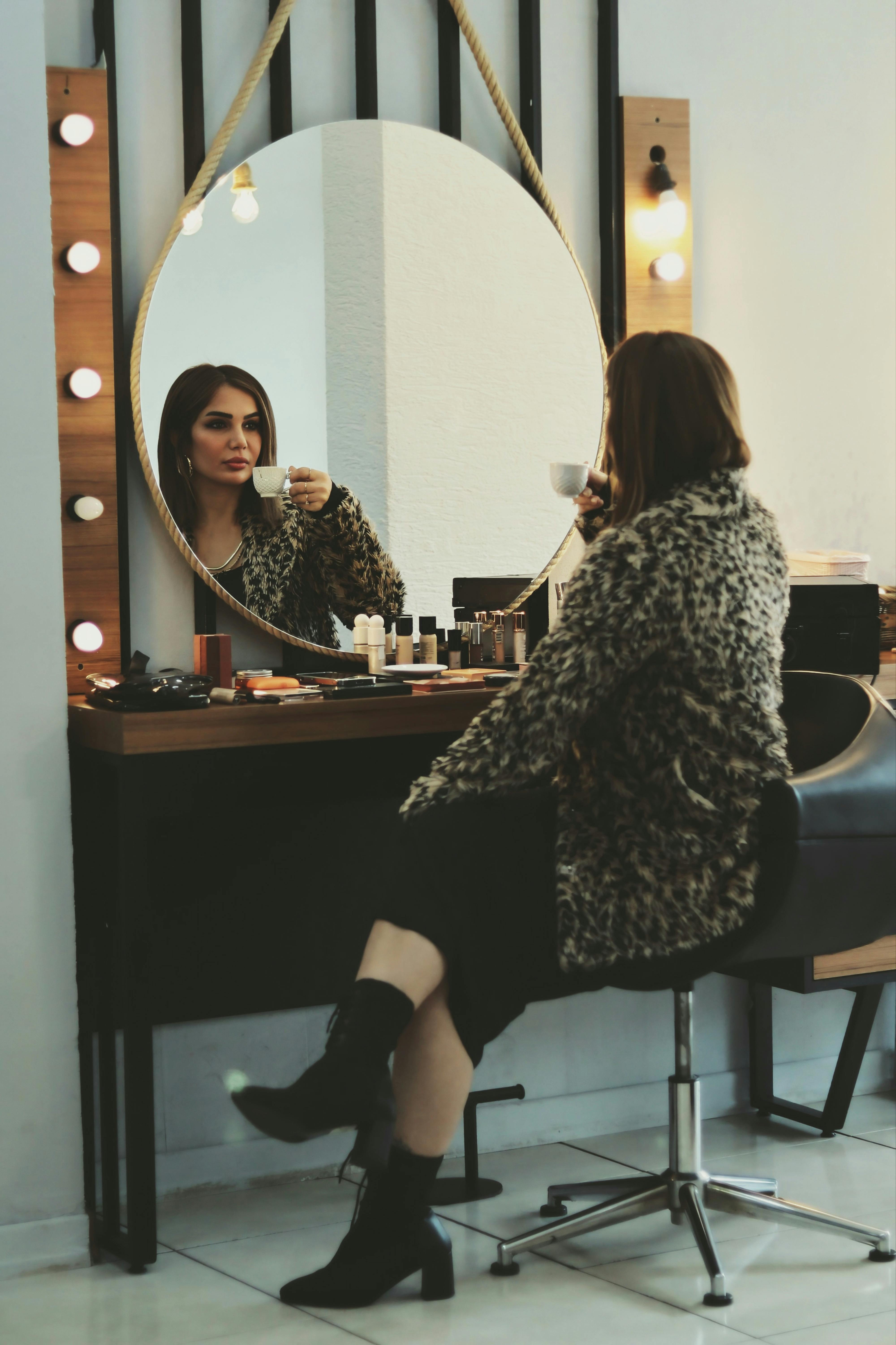 De franc Una dona amb un elegant abric amb estampat de lleopard pren cafè en un tocador elegant amb mirall de maquillatge. Foto d'estoc