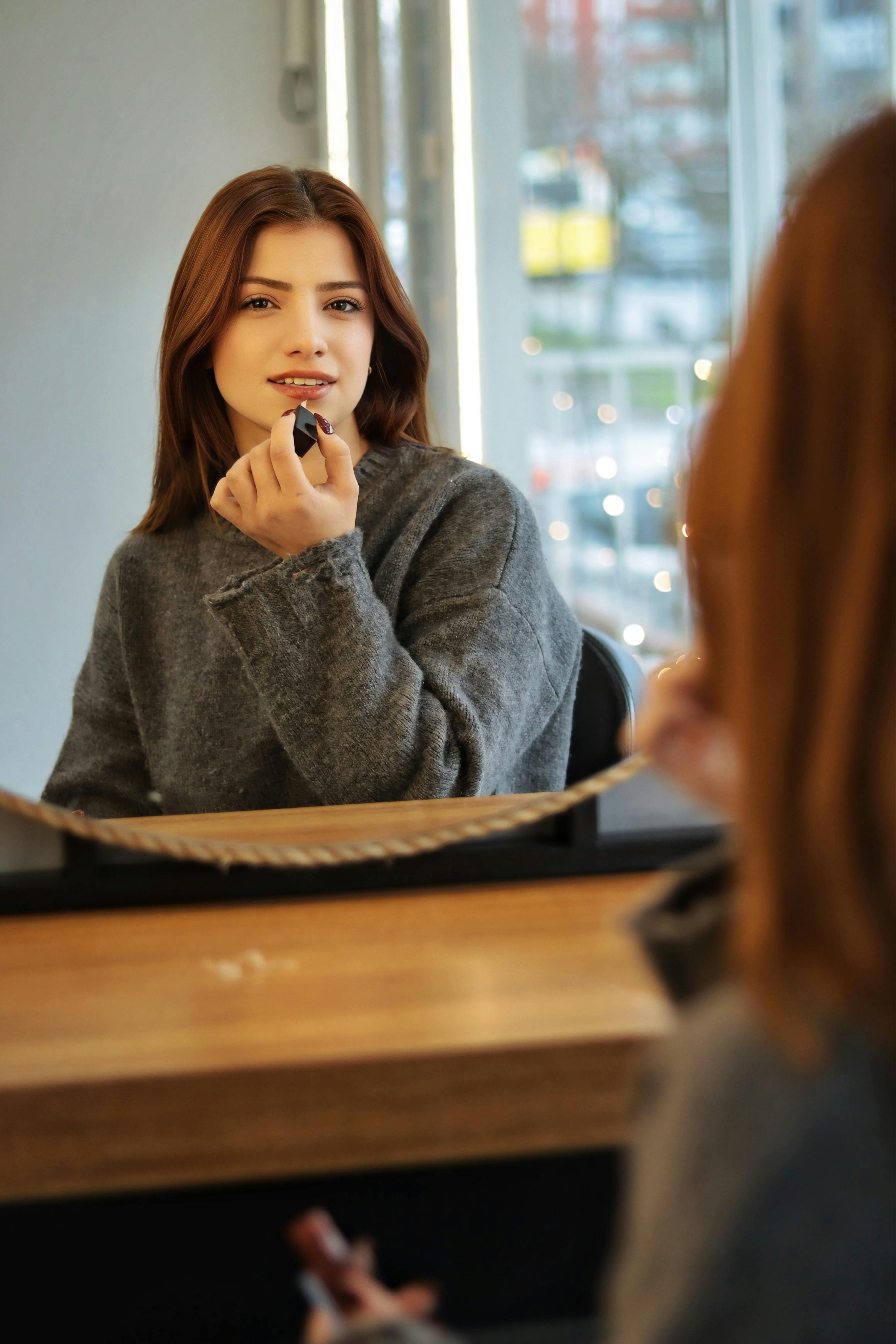 De franc Dona aplicant-se pintallavis davant d'un mirall a l'interior. Vista del paisatge urbà. Foto d'estoc