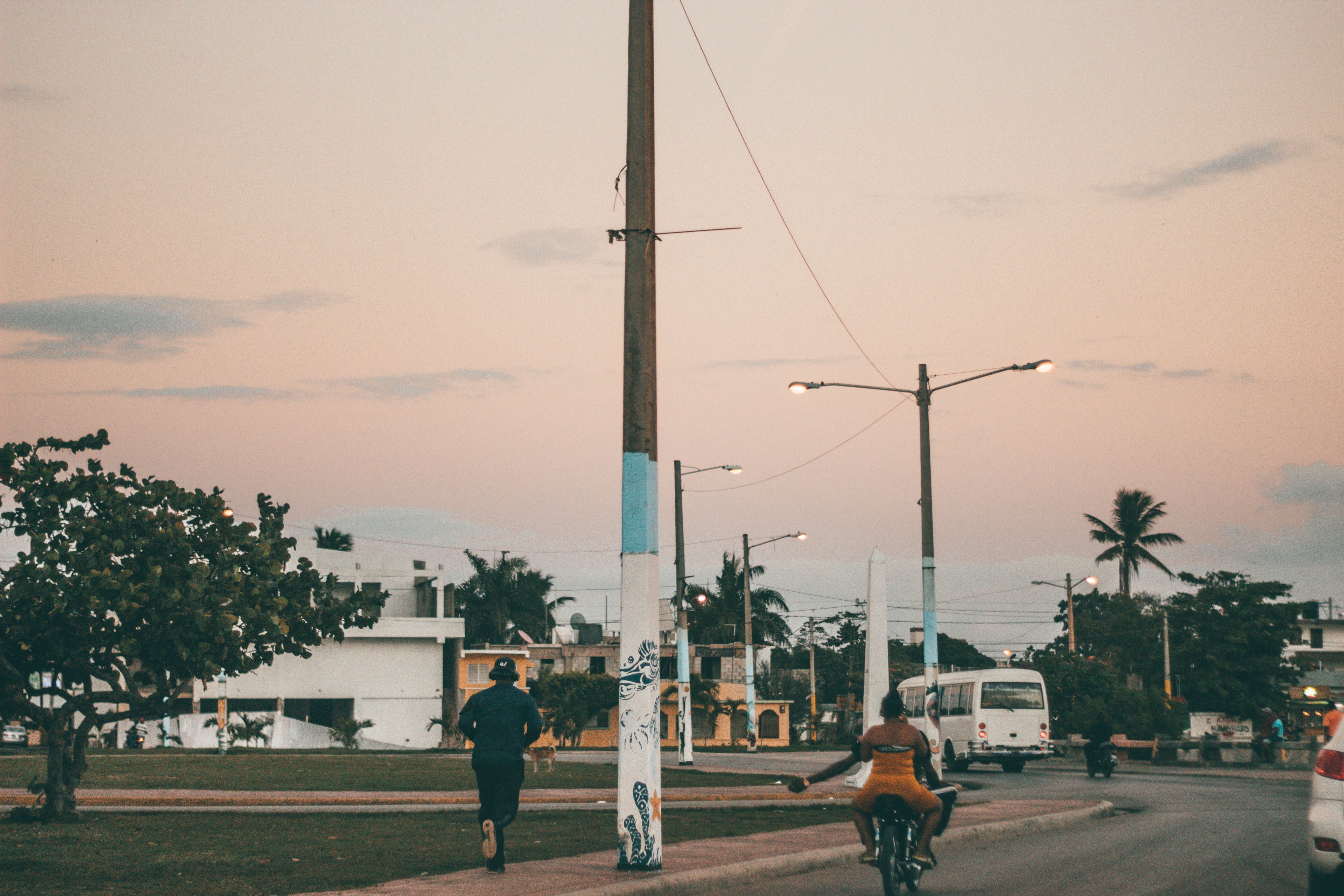Outdoor street scene with people on bikes and a white bus during sunset near buildings