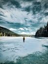 一个人走在广阔冰冻的湖面上，四周被白雪覆盖的树木包围