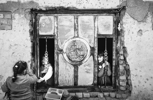 Children playing near a rustic window in Iraq, captured in black and white.
