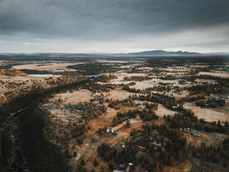 Drone view of rural neighborhoods with autumnal fields in trees under overcast sky