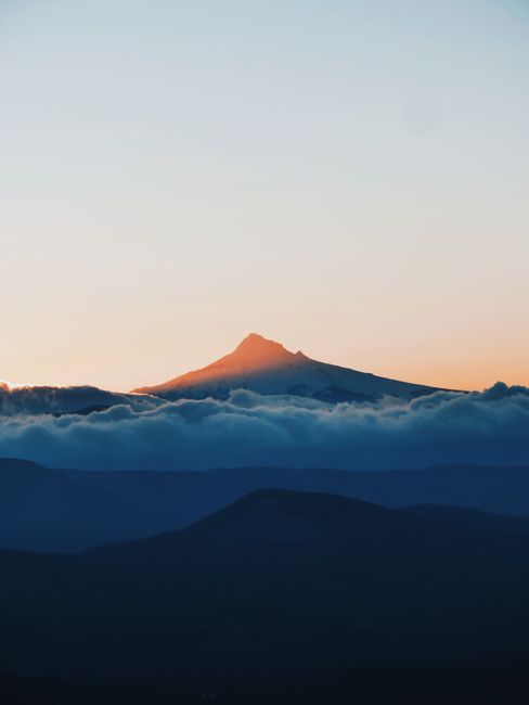 Breathtaking view of a mountain peak at sunrise with layers of clouds in a dramatic sky.