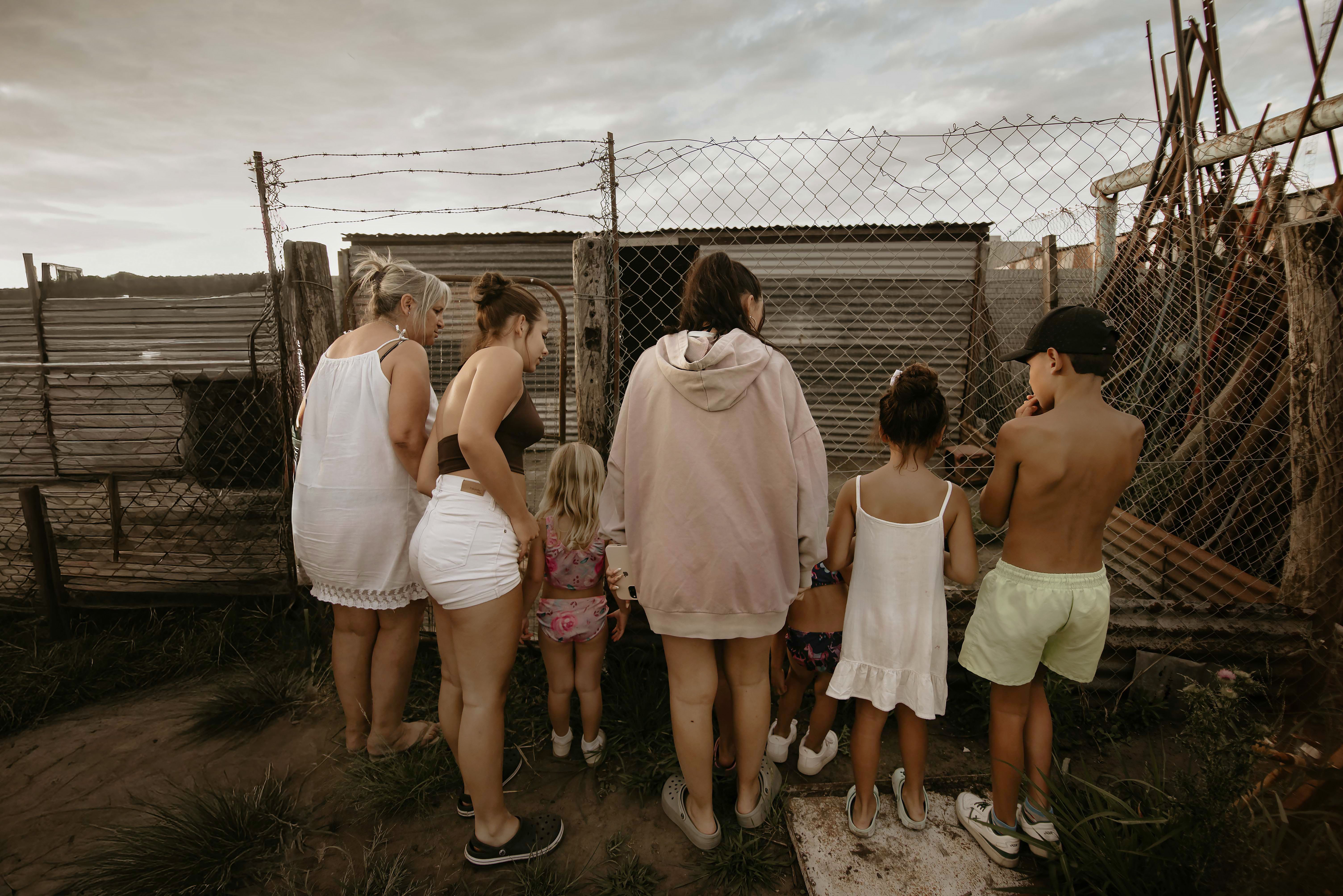 A diverse group of people gathered by a rural fence exploring the rustic surroundings outdoors.