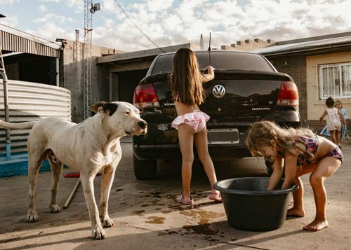 Free Two children wash a car in a sunny backyard with a dog nearby, creating a warm summer scene. Stock Photo