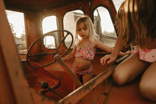 Free Two young girls explore inside a vintage tractor cabin, bathed in warm sunlight. Stock Photo