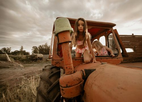 Free Two children explore a vintage tractor outdoors under a cloudy sky. Stock Photo
