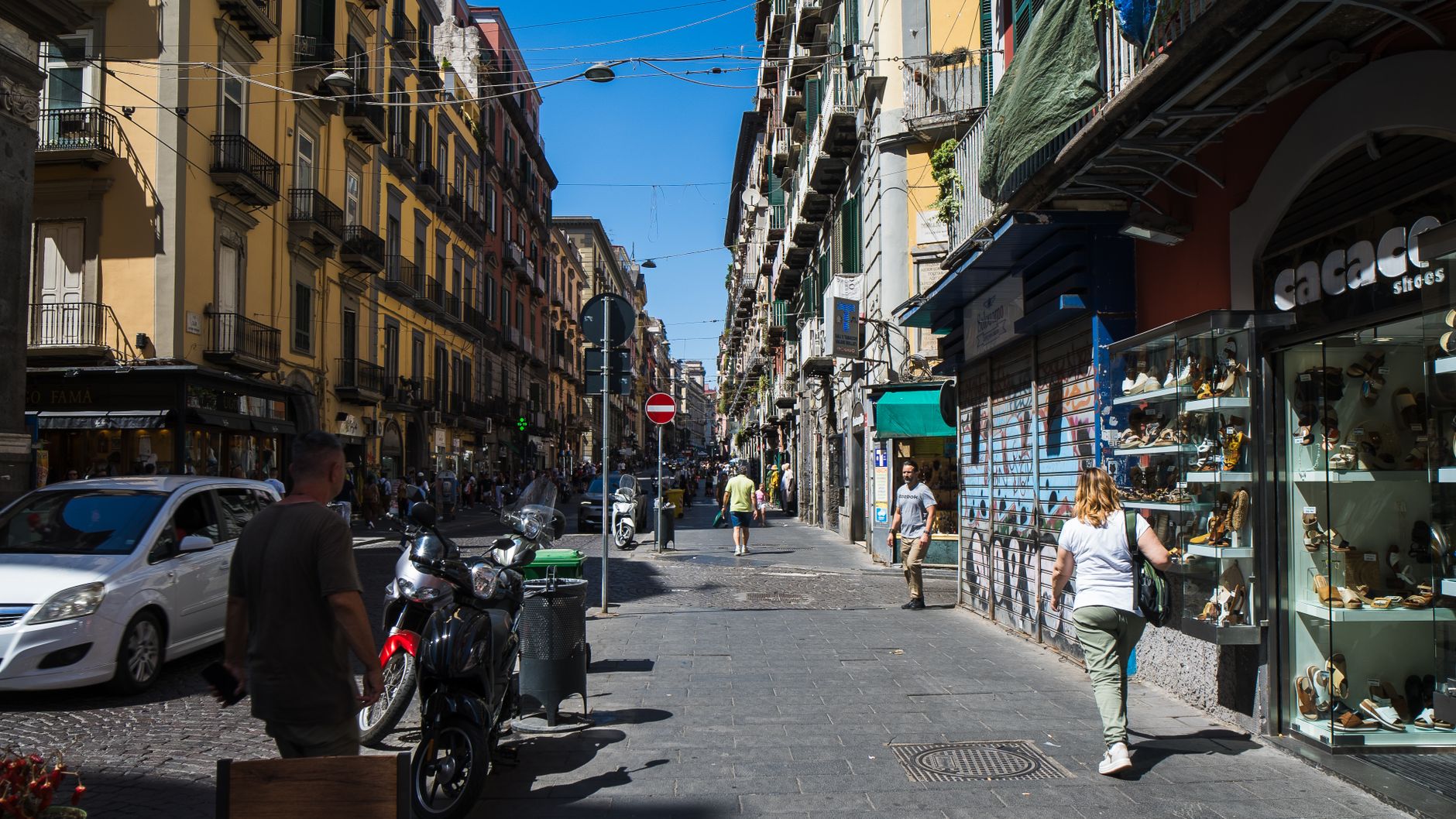Bustling street view in Naples with shops and pedestrians on a sunny day.