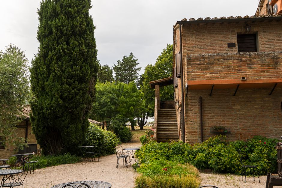 Charming rustic Italian courtyard featuring a brick building surrounded by lush greenery and outdoor seating.