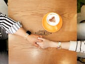 一对夫妇在咖啡馆里手牵手，俯视着心形拉花拿铁