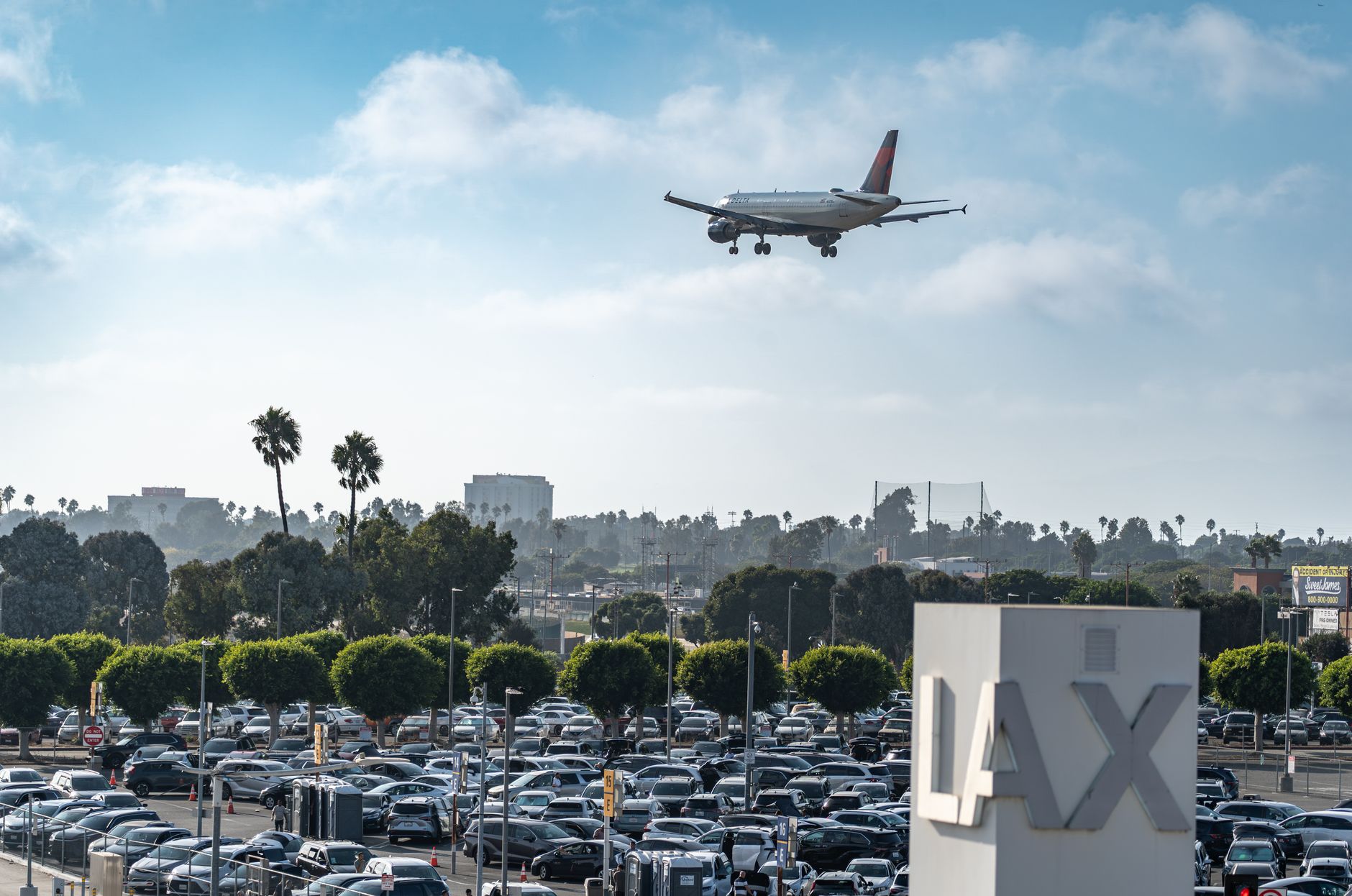 An aircraft on approach to LAX above the airport parking lots, just west of El Segundo