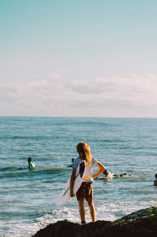 Free Young surfer holding a surfboard, looking at the ocean waves on a bright summer day. Stock Photo