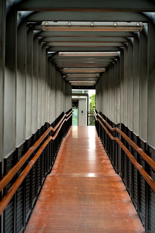 Free A modern industrial walkway with metal beams and wooden floorboards leading to a bright outdoor view. Stock Photo